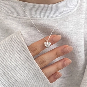 Close-up of silver heart pendant with pink and green zircon stones on a fine chain