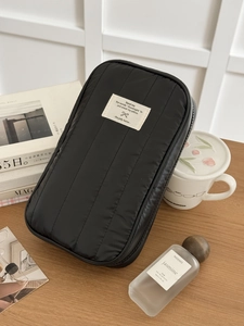 Borsa organizer da viaggio trapuntata nera verticale con etichetta su scrivania in legno