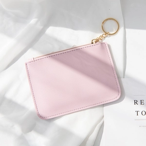 Pink lychee texture leather mini wallet with gold zipper and keychain on white fabric