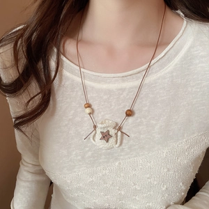 Detail of hand-woven white crochet pendant with wooden star and beads on necklace