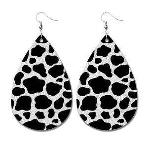 Detail of drop-shaped PU leather earrings featuring a black and white cow print pattern