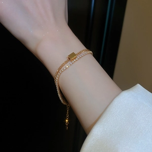 Detailed close-up of a double-layer gold chain bracelet with zircon and square pendant