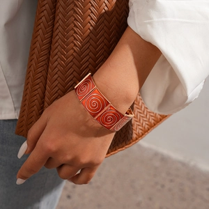 Detail of wide gold enamel bracelet with orange spiral texture worn by fashion model