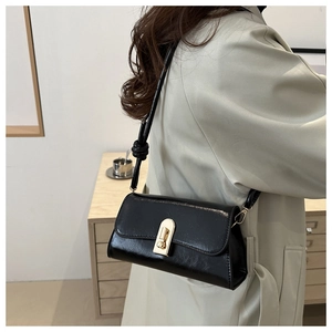 Detail of a black glossy leather baguette bag with a golden metal twist lock on a beige coat