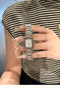 Detail shot of a silver square watch dial with a date window and chain link steel strap