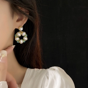 Dettaglio di orecchini vintage dorati con perle e pietre turchesi indossati dal modello