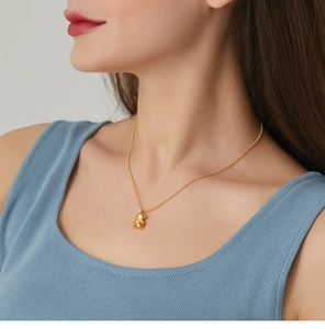 Close-up of golden 3D bear pendant on ball chain worn by a model in a blue ribbed top