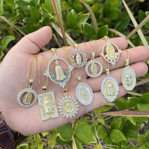Gold plated Virgin Mary pendants with cubic zirconia held by hand outdoors