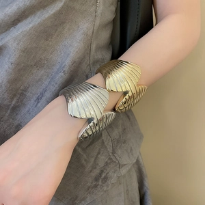 Detail of a gold and silver wide open cuff bracelet with seashell texture on a female wrist