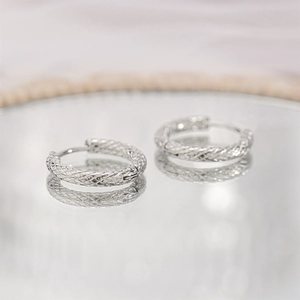 Macro shot of silver textured hoop earrings with woven design on reflective surface