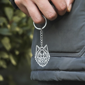 Modern stainless steel keychain featuring a geometric wolf head pendant held in hand
