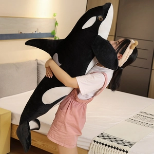 Woman hugging a giant black and white orca plush pillow in a cozy bedroom setting