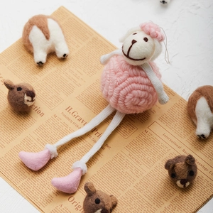 Pink curly wool felt sheep doll with long legs and heart-shaped feet on vintage paper