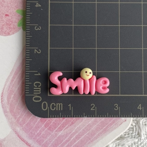 Macro shot of a pink resin 'Smile' charm with a yellow face on a ruler cutting mat