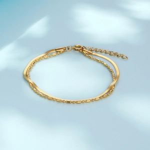 Double-layered gold snake chain and bead bracelet on a soft blue background