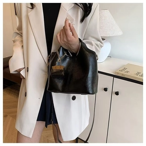 Detail of classic black wax leather tote bag with gold chain strap on white blazer