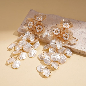 Elegant gold flower tassel earrings with white pearls on textured stone background