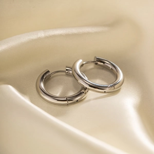 Polished silver stainless steel hoop earrings on champagne satin background