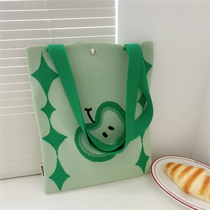 Detail of green knit tote bag featuring woven apple patterns and silver magnetic clasp