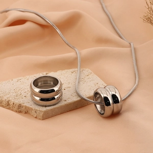 Ensemble collier chaîne serpent et double bague argenté sur un socle en pierre beige