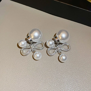 Macro view of double pearl earrings with sparkling crystal bow link on beige texture