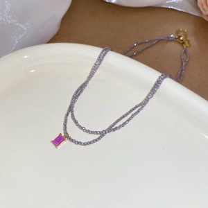 Close-up of purple beaded necklace with a gold-set rectangular crystal pendant