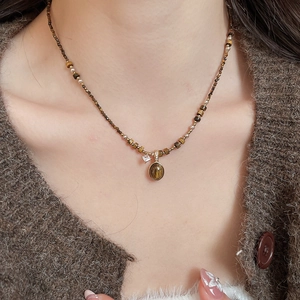 Detailed view of beaded tiger eye necklace with gold charm on a female model