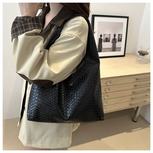 Close-up of black woven leather tote bag worn by model in a minimalist home setting