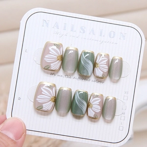 Macro detail of handmade cat-eye press-on nails with daisy art and gold trim