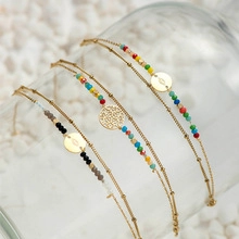 Detail of colorful beaded necklaces on a glass bottle with white pebble background