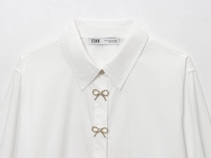 Dettaglio camicia bianca in popeline con bottone fiocco strass ed etichetta taglia S