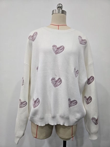 Detail of white knit sweater featuring delicate fuchsia heart embroidery on chest