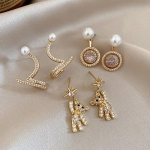 Macro detail of three gold earrings with pearls and rhinestones on silk fabric background