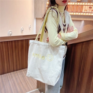 Close-up of white canvas tote with yellow smile embroidery and unique beaded shoulder strap