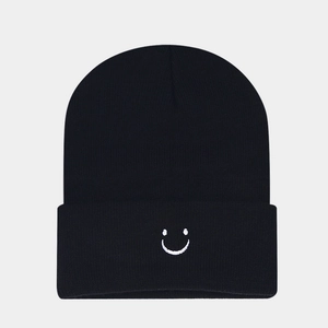 Detailed view of black knitted beanie with white embroidered smiley face on cuffed brim