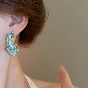 Close-up of C-shaped aquamarine beaded earrings with gold accents worn by a model
