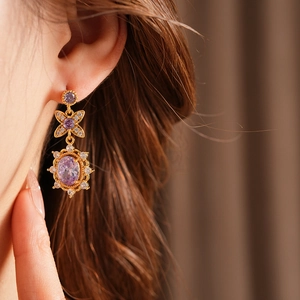 Close-up of vintage style gold earrings with oval purple gemstones and zircon crystals