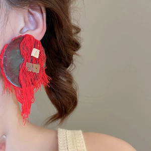 Macro detail of red fringe earrings with golden square sequins and a large round base