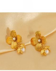Detailed close-up of golden flower pearl earrings on satin fabric background