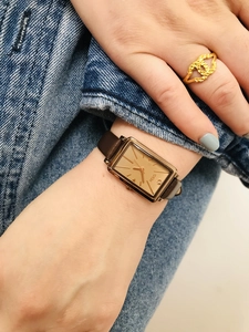 Close-up of GEDI rectangular gold watch with brown leather strap on female wrist