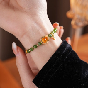 Detail of beaded bracelet with green jade beads and an orange gourd pendant on a wrist