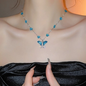 Detalle del collar con colgante de mariposa azul y perlas blancas en cadena de plata