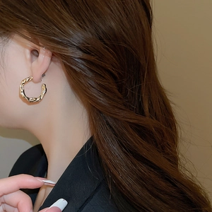 Close-up of golden C-shaped twisted earrings with hammered texture and small zircons on ear