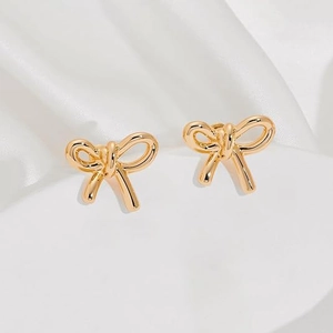 Detail shot of golden bow knot earrings on elegant white silk fabric background