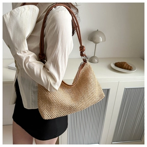 Chic beige woven straw shoulder bag with brown leather strap worn in a cozy home setting