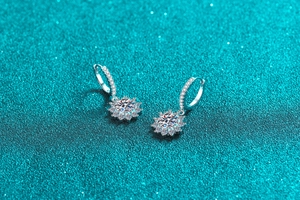 Macro shot of silver sunflower earrings with moissanite stones on sparkling teal background