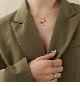 Close-up of golden dolphin pendant necklace and layered rings on model with green blazer