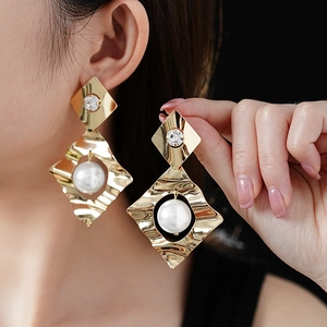 Detailed view of wavy gold metal earrings with large white pearl and sparkling crystals