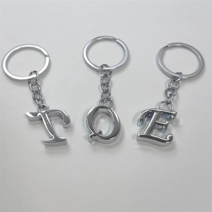 Minimalist silver metal alphabet keychains with polished letters T, Q, and E on white background