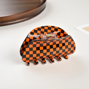 Macro shot of large orange and black checkerboard hair claw clip with golden metal spring